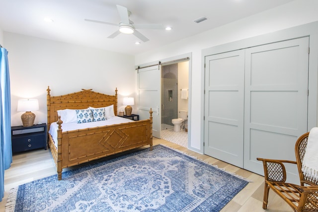 bedroom featuring ensuite bathroom, wood-type flooring, ceiling fan, a barn door, and a closet