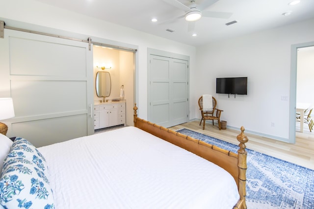 bedroom with ceiling fan, ensuite bathroom, a barn door, and light hardwood / wood-style floors