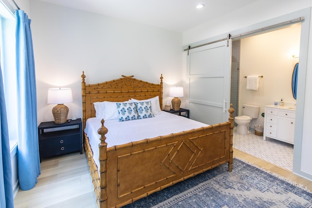 bedroom featuring wood-type flooring, a barn door, and connected bathroom