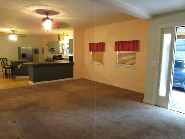 unfurnished living room with beamed ceiling, ceiling fan, and carpet