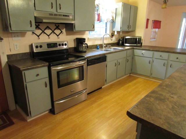 kitchen with sink, appliances with stainless steel finishes, green cabinetry, kitchen peninsula, and light wood-type flooring