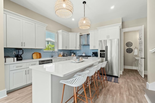 kitchen with stainless steel appliances, a kitchen island, white cabinets, and wall chimney exhaust hood