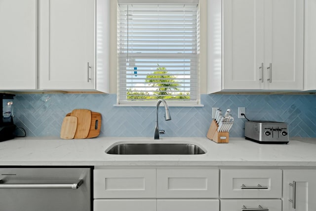 kitchen featuring white cabinetry, sink, stainless steel dishwasher, and light stone countertops