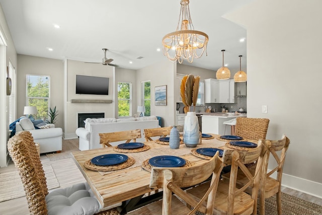 dining room with a healthy amount of sunlight, ceiling fan with notable chandelier, and light hardwood / wood-style floors