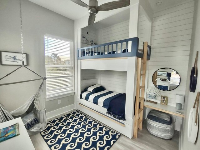 bedroom featuring hardwood / wood-style flooring, wooden walls, and ceiling fan