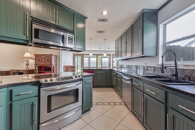 kitchen with sink, a textured ceiling, light tile patterned floors, green cabinets, and stainless steel appliances