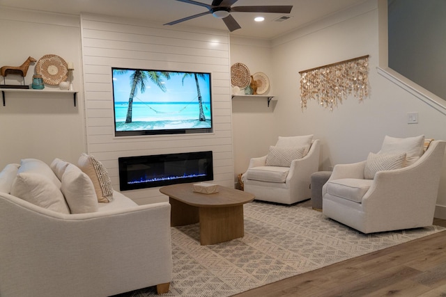 living room featuring crown molding, light hardwood / wood-style flooring, a large fireplace, and ceiling fan