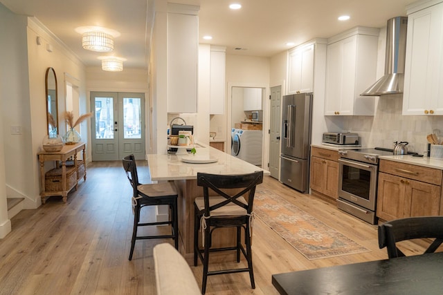 kitchen featuring wall chimney range hood, washer / dryer, stainless steel appliances, and white cabinets