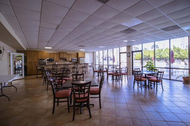 dining space with light tile patterned flooring, a wall of windows, and a drop ceiling