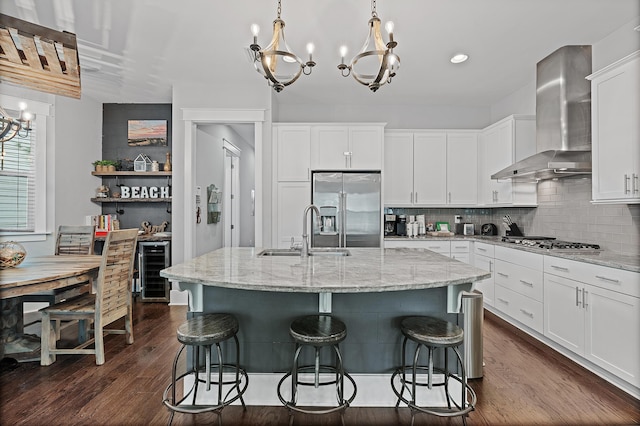 kitchen featuring stainless steel appliances, sink, a center island with sink, and wall chimney range hood