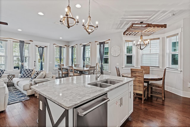 kitchen with an island with sink, sink, hanging light fixtures, stainless steel dishwasher, and light stone counters