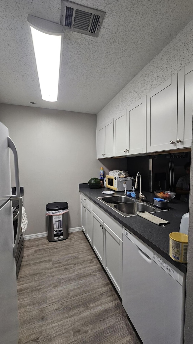 kitchen featuring dishwasher, sink, white cabinets, hardwood / wood-style flooring, and a textured ceiling