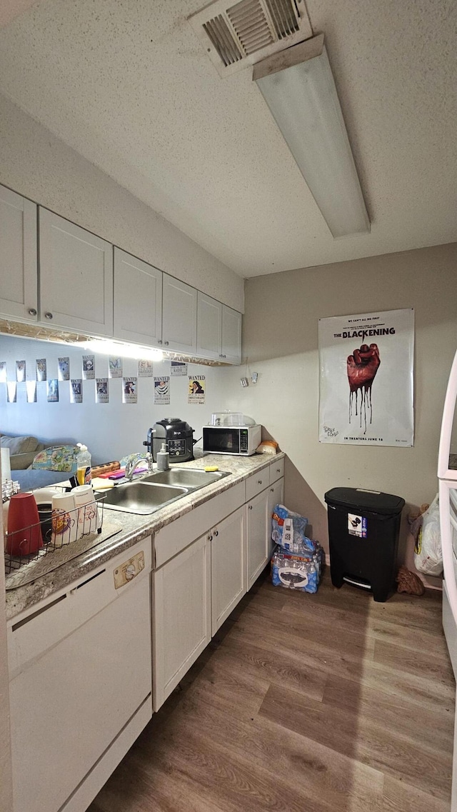 kitchen featuring sink, hardwood / wood-style floors, white dishwasher, a textured ceiling, and white cabinets