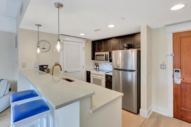 kitchen with sink, a kitchen breakfast bar, hanging light fixtures, kitchen peninsula, and stainless steel appliances