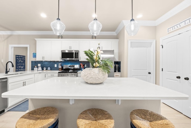 kitchen with appliances with stainless steel finishes, pendant lighting, white cabinetry, sink, and a kitchen breakfast bar