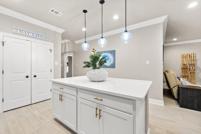 kitchen with ornamental molding, white cabinets, a kitchen island, decorative light fixtures, and light wood-type flooring