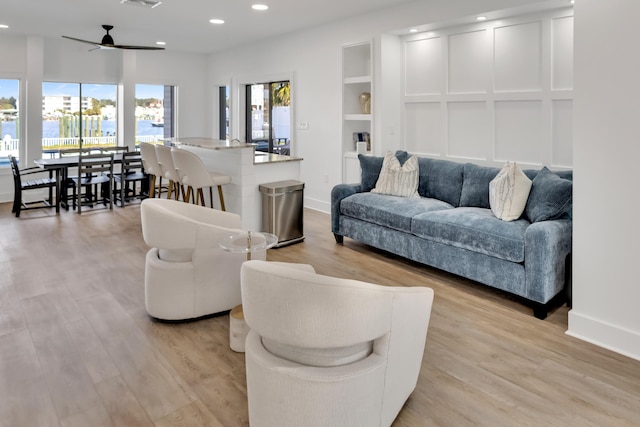 living room with light hardwood / wood-style flooring, ceiling fan, and built in shelves