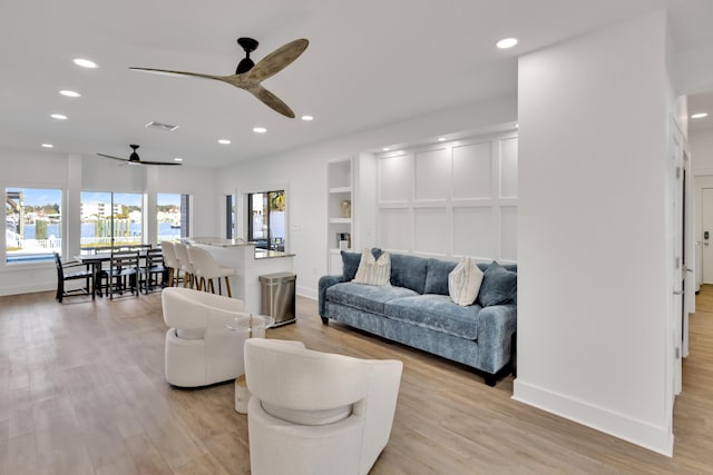 living room with built in shelves, ceiling fan, and light wood-type flooring