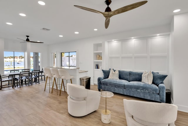 living room featuring ceiling fan, built in features, and light hardwood / wood-style floors