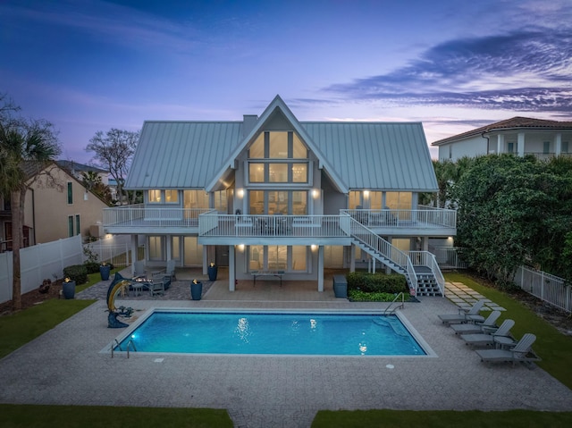 back house at dusk with a fenced in pool, a balcony, and a patio area