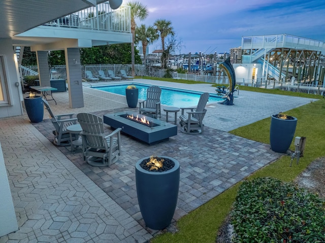 pool at dusk featuring a fire pit, a patio, and a water view