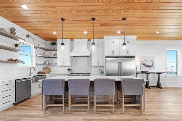 kitchen with premium range hood, a kitchen island, pendant lighting, and appliances with stainless steel finishes