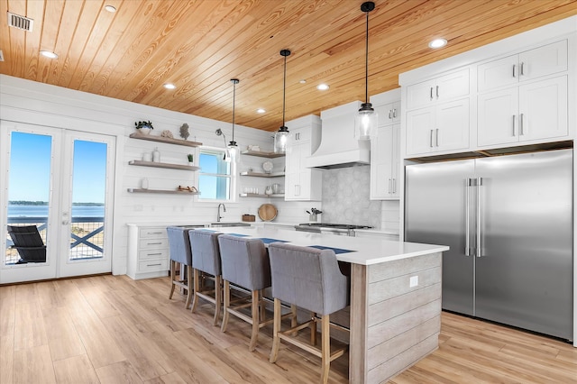 kitchen featuring a water view, white cabinets, a kitchen island, custom exhaust hood, and stainless steel built in fridge