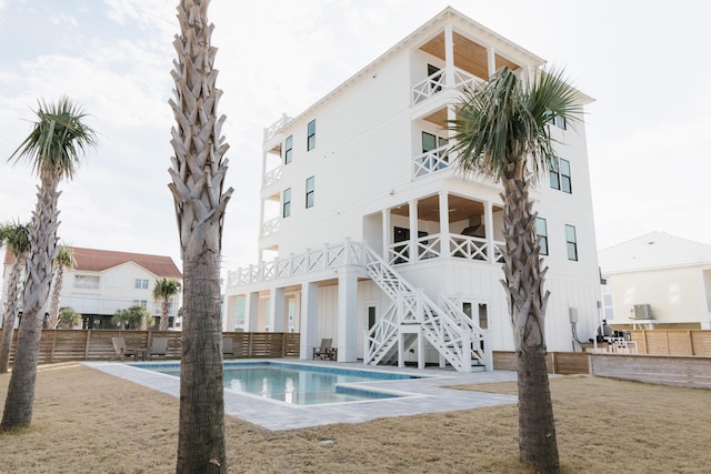 rear view of house featuring a balcony, a community pool, and a lawn