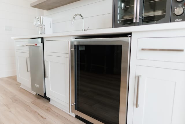 bar with wine cooler, white cabinetry, and light hardwood / wood-style floors