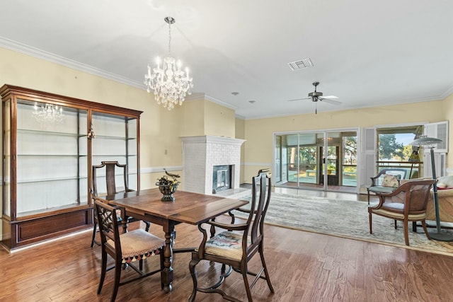 dining room featuring hardwood / wood-style floors, crown molding, a fireplace, and ceiling fan with notable chandelier