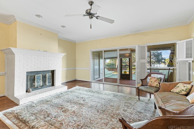 living room with dark wood-type flooring, ceiling fan, ornamental molding, and a fireplace