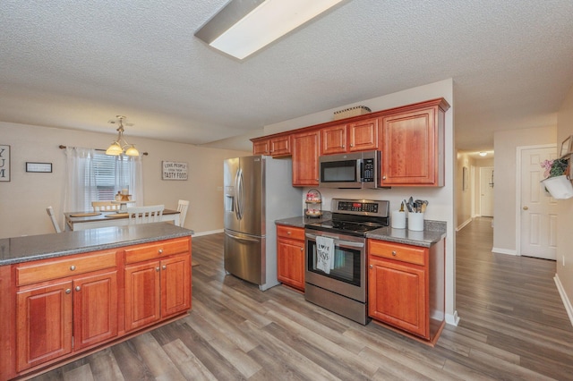 kitchen featuring pendant lighting, hardwood / wood-style floors, stainless steel appliances, and a textured ceiling