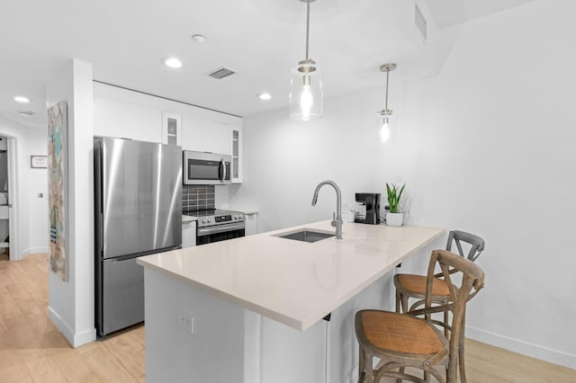 kitchen with sink, a breakfast bar area, hanging light fixtures, appliances with stainless steel finishes, and white cabinets