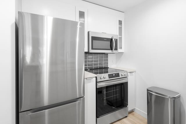 kitchen featuring backsplash, stainless steel appliances, light hardwood / wood-style floors, and white cabinets