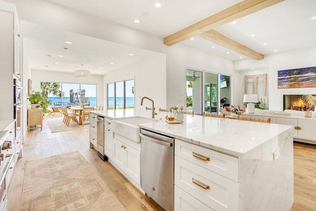 kitchen featuring a large island, sink, a water view, light stone counters, and stainless steel dishwasher