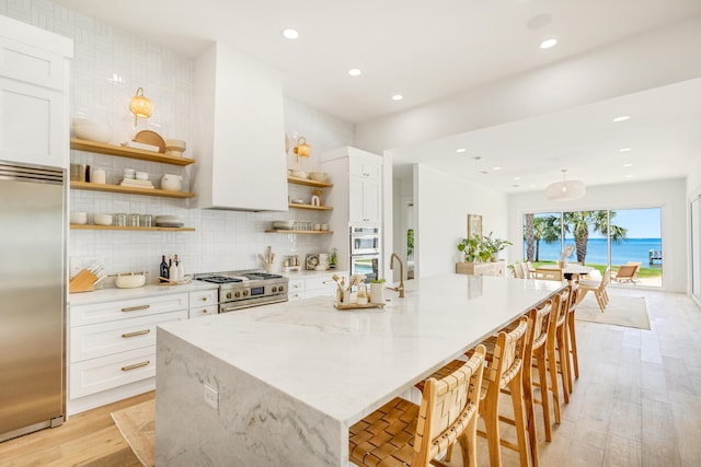 kitchen featuring light stone countertops, stainless steel appliances, white cabinets, and a water view