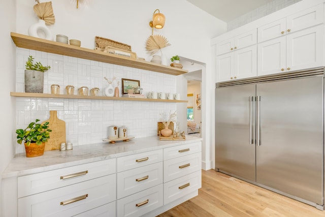 kitchen featuring white cabinetry, light stone counters, tasteful backsplash, light hardwood / wood-style floors, and built in fridge