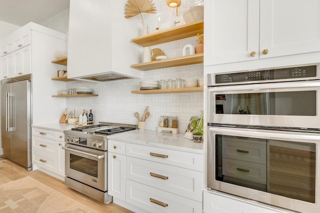 kitchen featuring white cabinetry, light stone counters, premium appliances, and decorative backsplash