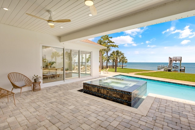 view of pool featuring an in ground hot tub, a water view, ceiling fan, and a patio area