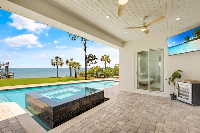 view of swimming pool with an in ground hot tub, a water view, ceiling fan, and a patio area