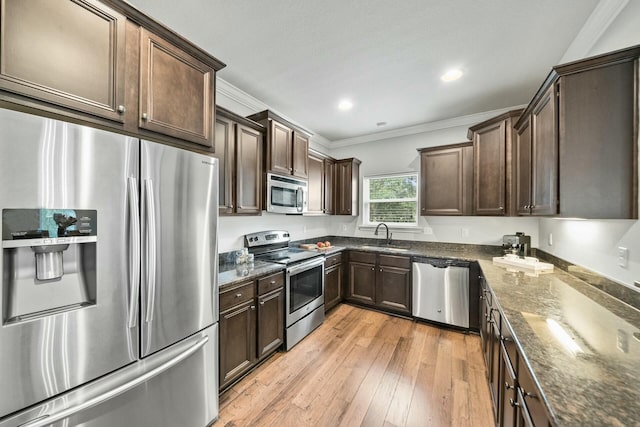 kitchen featuring appliances with stainless steel finishes, sink, dark stone counters, ornamental molding, and light hardwood / wood-style flooring