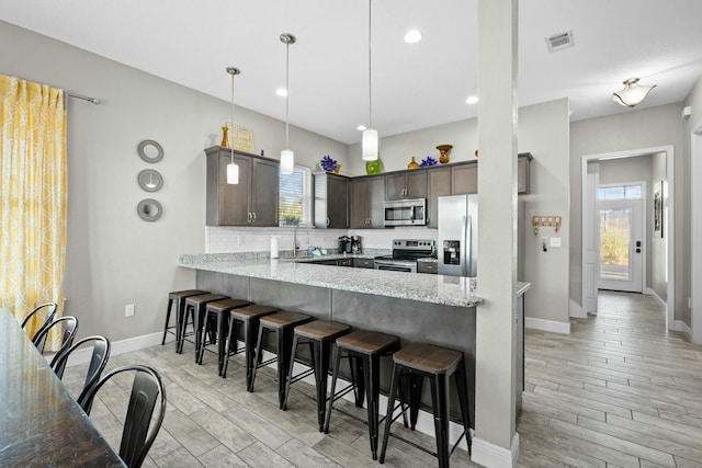 kitchen featuring appliances with stainless steel finishes, pendant lighting, sink, kitchen peninsula, and dark brown cabinets