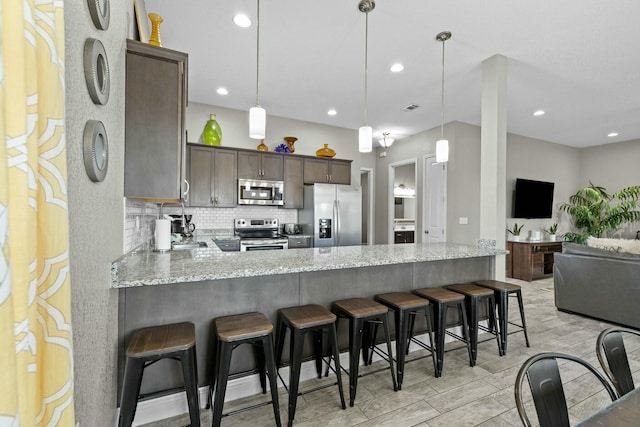 kitchen featuring decorative backsplash, stainless steel appliances, kitchen peninsula, and hanging light fixtures