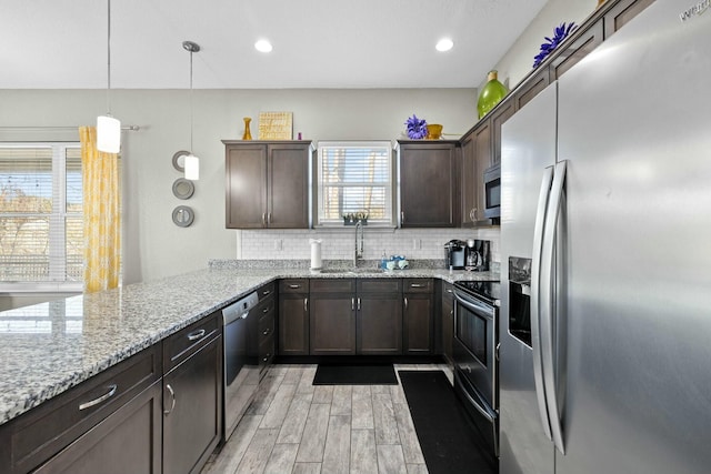 kitchen featuring sink, hanging light fixtures, stainless steel appliances, light stone counters, and kitchen peninsula