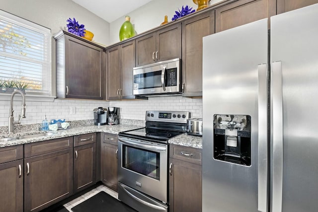 kitchen featuring dark brown cabinetry, appliances with stainless steel finishes, light stone countertops, and sink