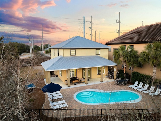 back house at dusk featuring a fenced in pool and a patio