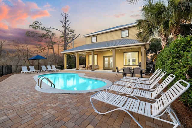 pool at dusk with french doors and a patio area