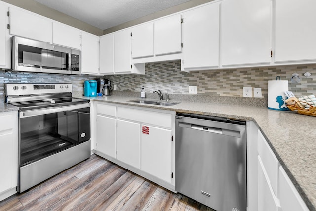 kitchen featuring white cabinetry, sink, backsplash, light hardwood / wood-style floors, and stainless steel appliances