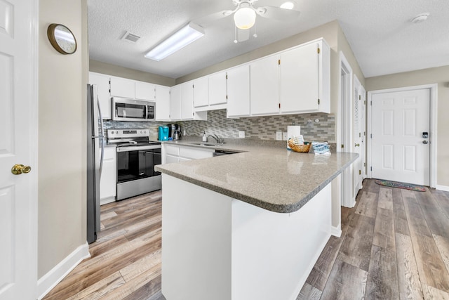 kitchen with sink, appliances with stainless steel finishes, white cabinetry, kitchen peninsula, and light wood-type flooring