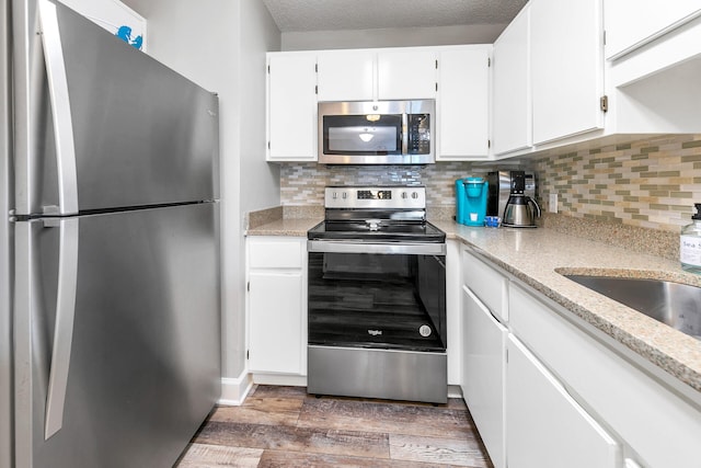 kitchen with tasteful backsplash, appliances with stainless steel finishes, dark hardwood / wood-style flooring, light stone countertops, and white cabinets